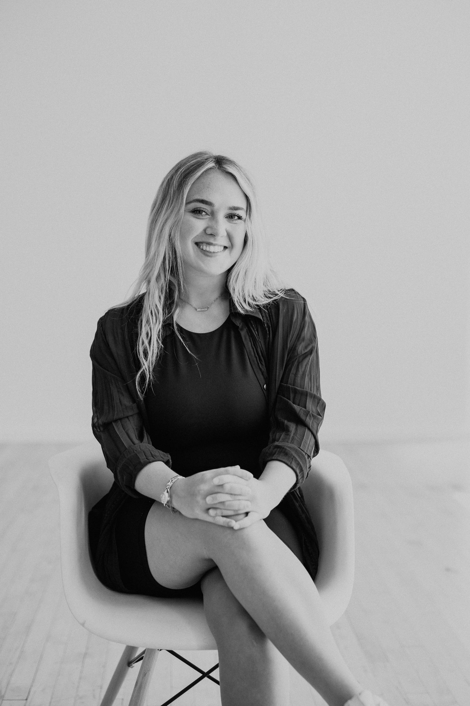 A person in black attire sitting on a modern chair against a light background.