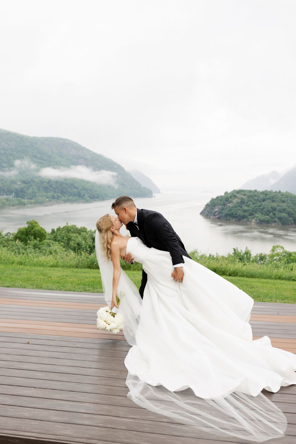 Romantic wedding photos on a wooden deck with flowing white dress and dramatic mountain lake backdrop.