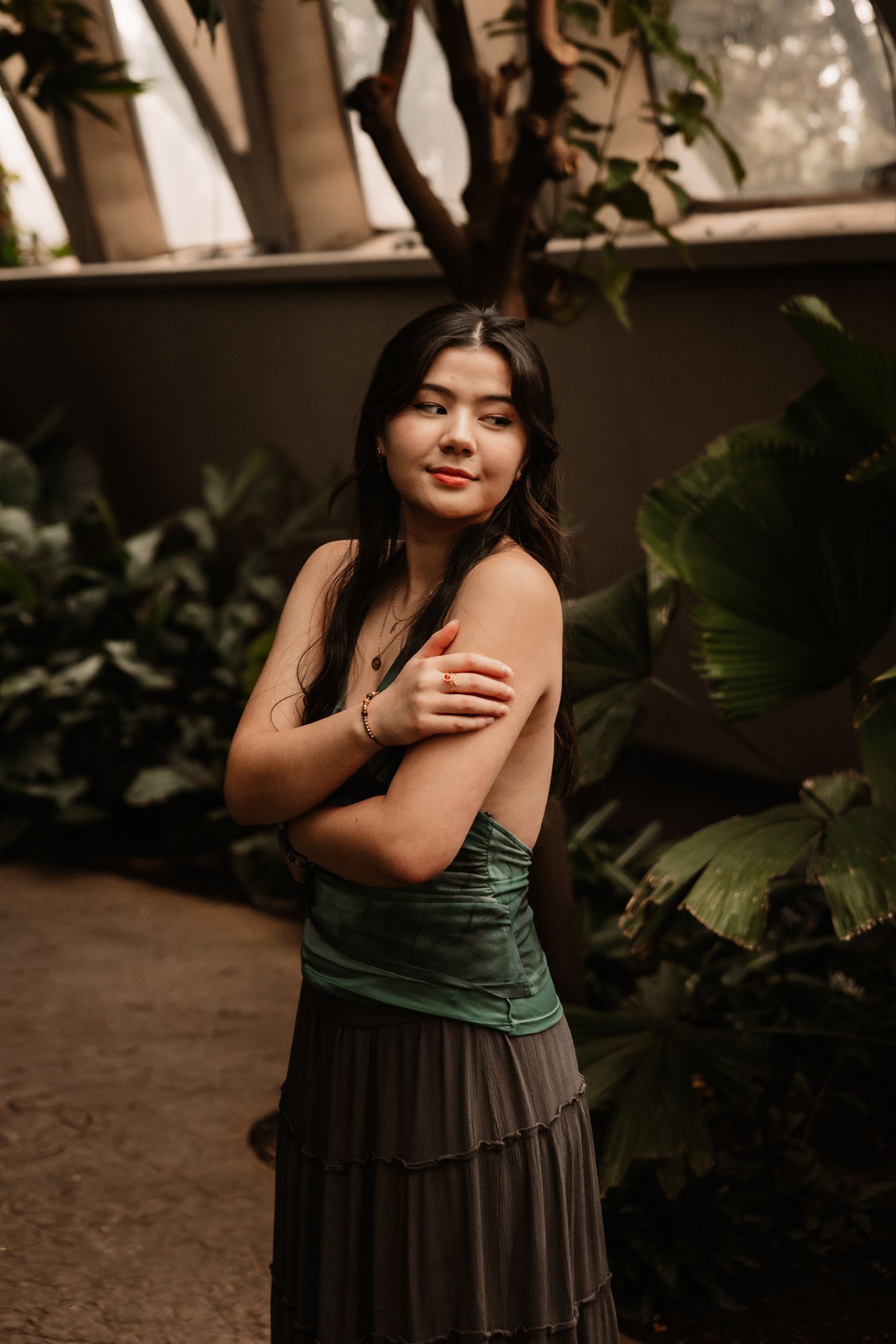 A casual outdoor portrait of someone in a floral tank top and jeans sitting on rocks among foliage.