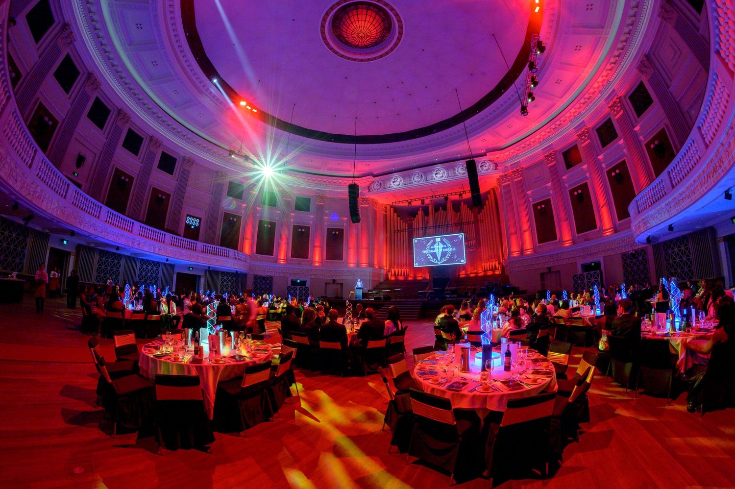 Stunning circular venue bathed in red and purple lighting with elegant table settings.