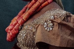 Photography Oil painting Detail shot of coral necklaces and silver embellishments on beige fabric worn by a Rivers bride.