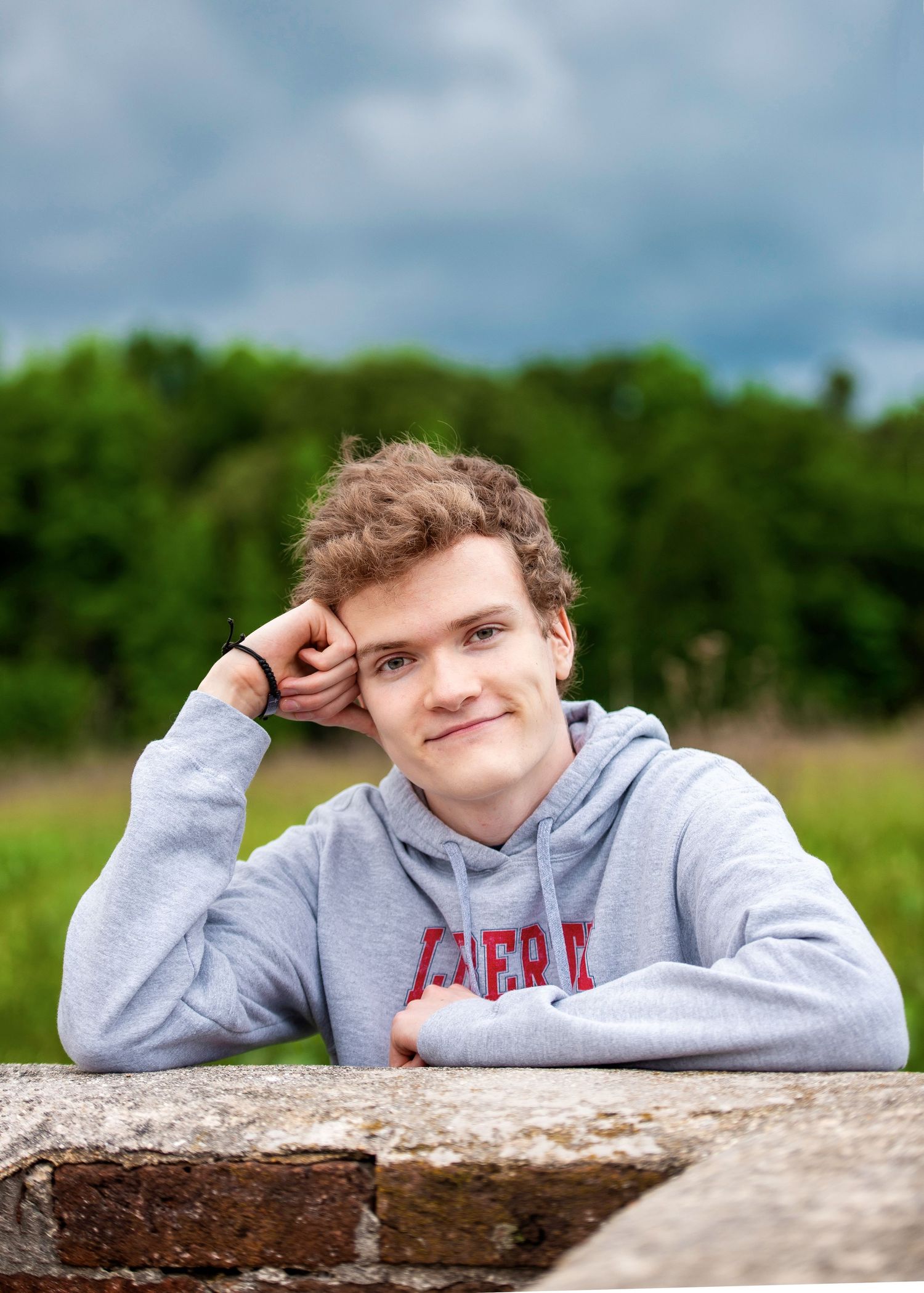 Casual outdoor portrait leaning on stone wall in grey hoodie.