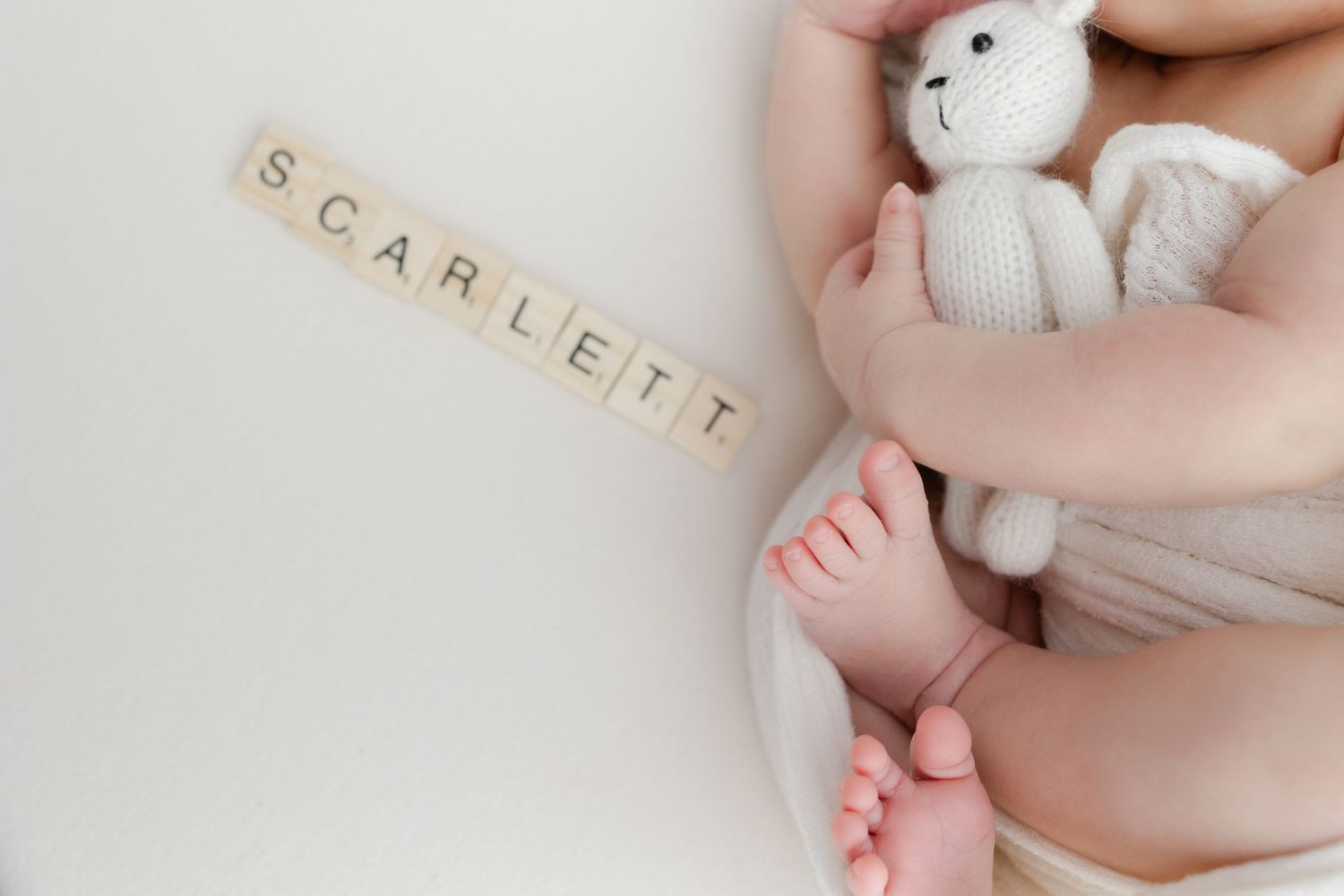 Small plush bunny toy next to wooden letter tiles spelling 'Scarlett' with baby feet visible.