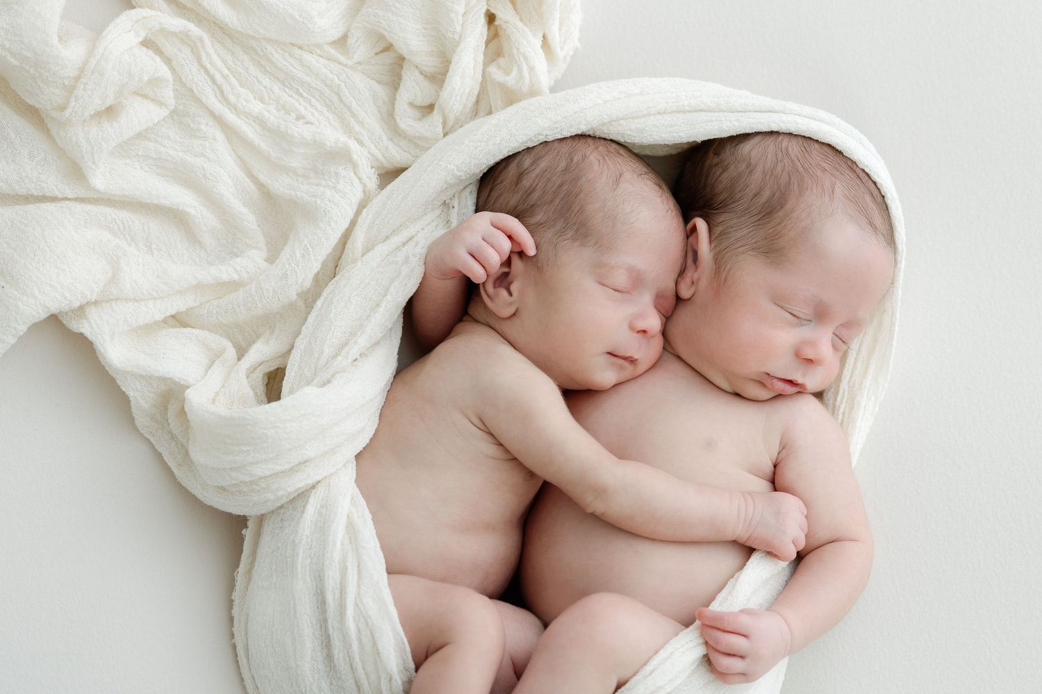 Collage of newborn babies sleeping peacefully on white blankets in various poses.