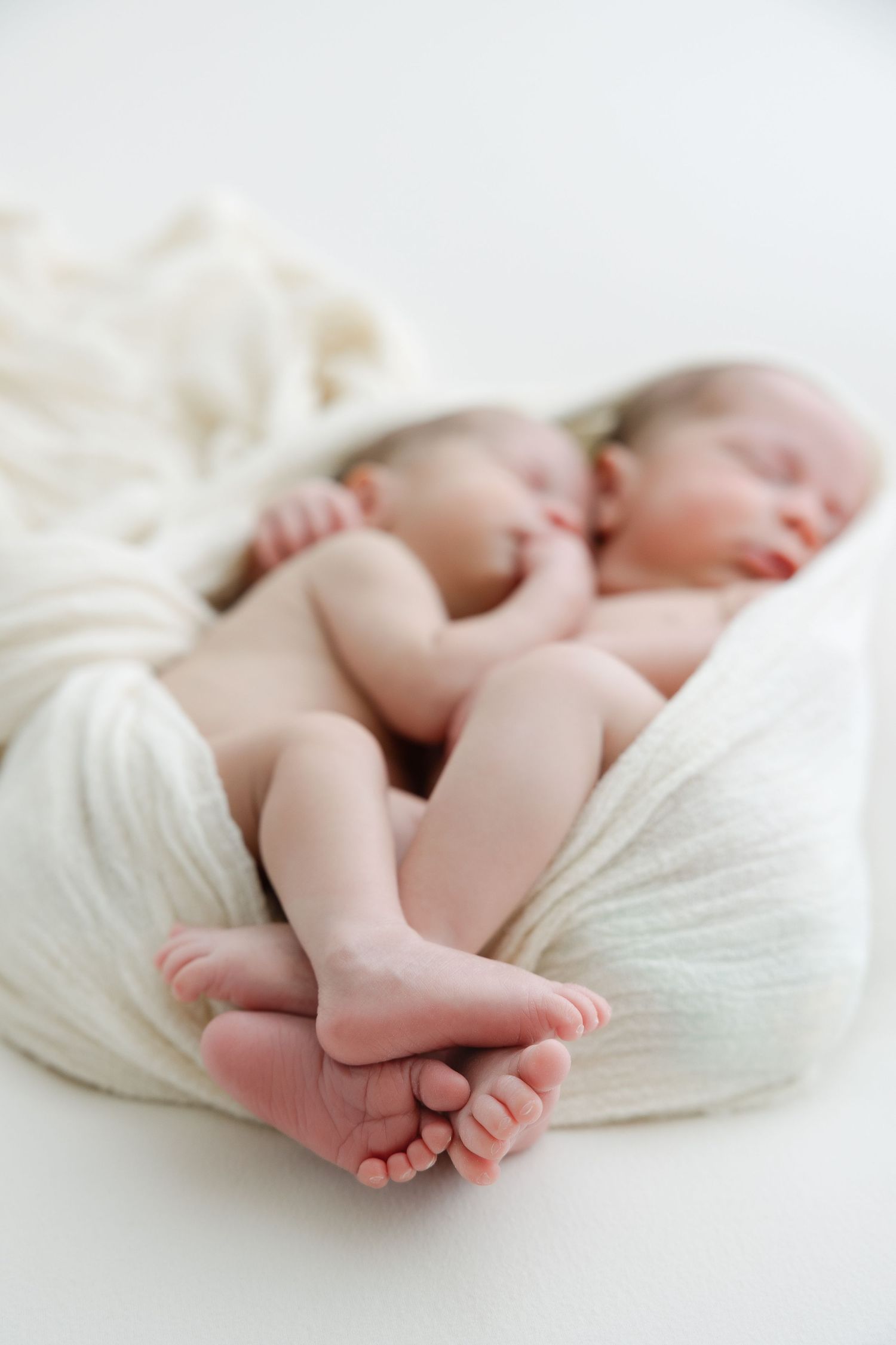 Three artistic newborn baby photos showing tiny feet and legs wrapped in soft white fabric against a light background.