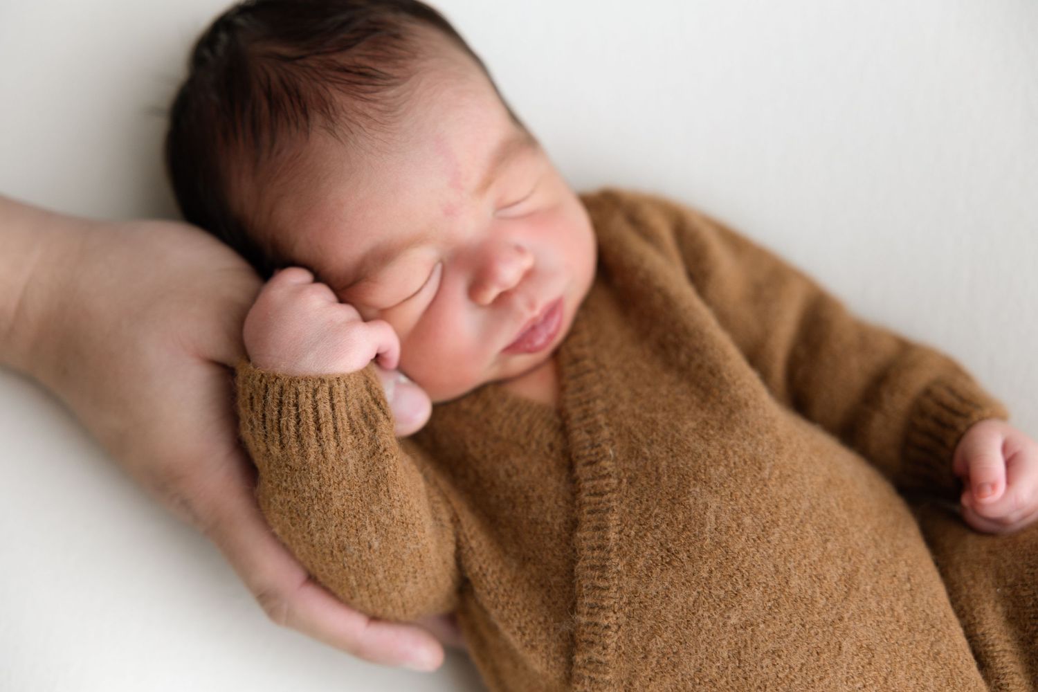 A series of hands gently folding a soft brown knit fabric in different positions.