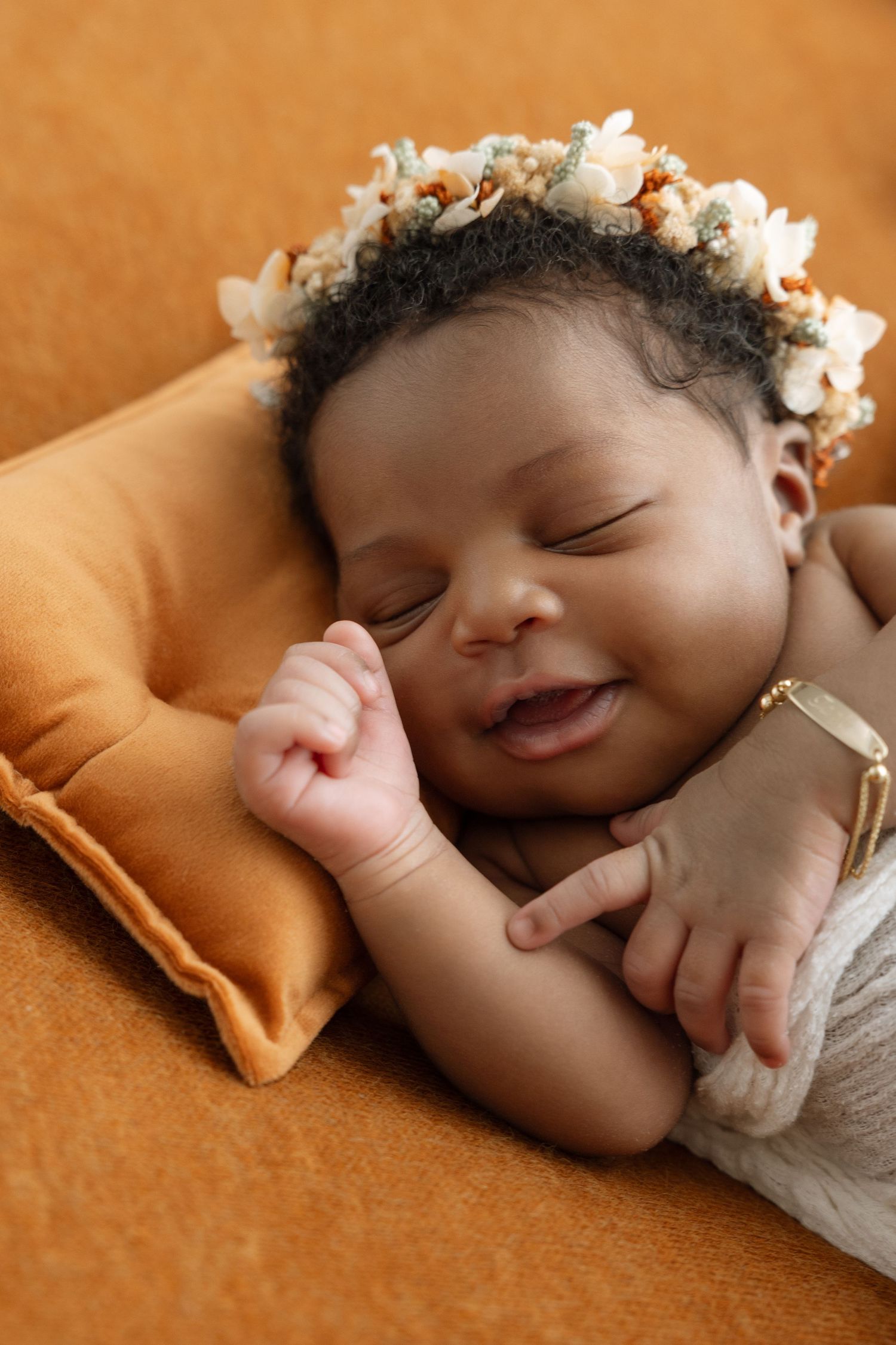 Sleeping baby with flower crown lying on brown blanket in peaceful slumber.