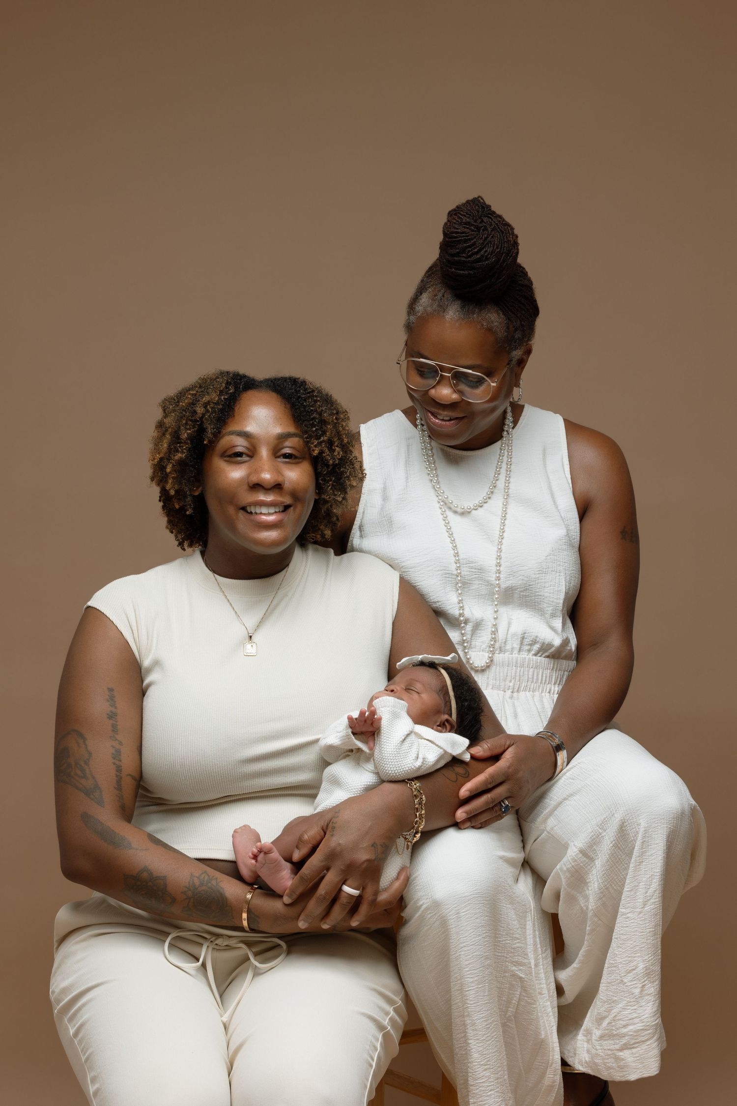 A couple in matching white outfits sits together on a brown backdrop in a series of intimate portrait photos.