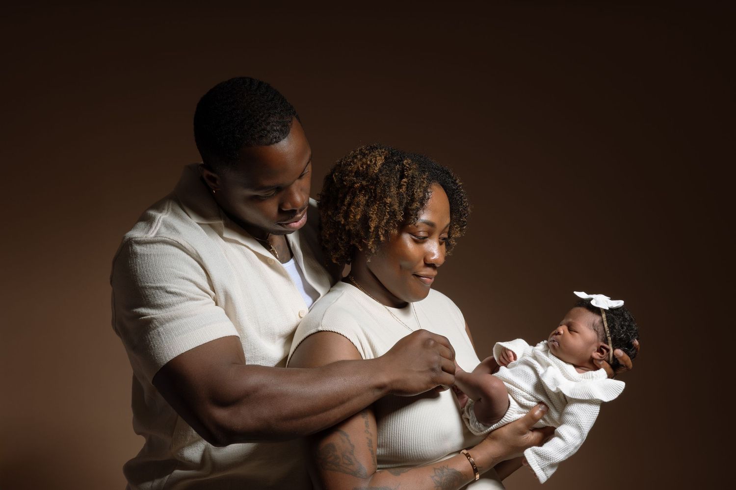 A series of tender moments between parents and their newborn baby shown in warm brown tones against a dark background.