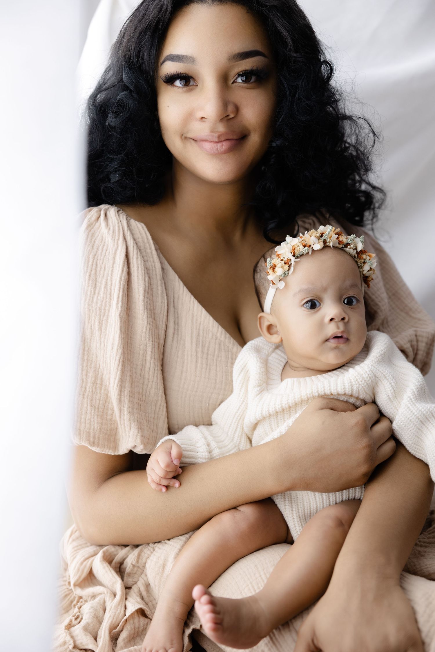 A parent and baby wearing matching cream colored outfits pose together in a series of tender studio portraits.