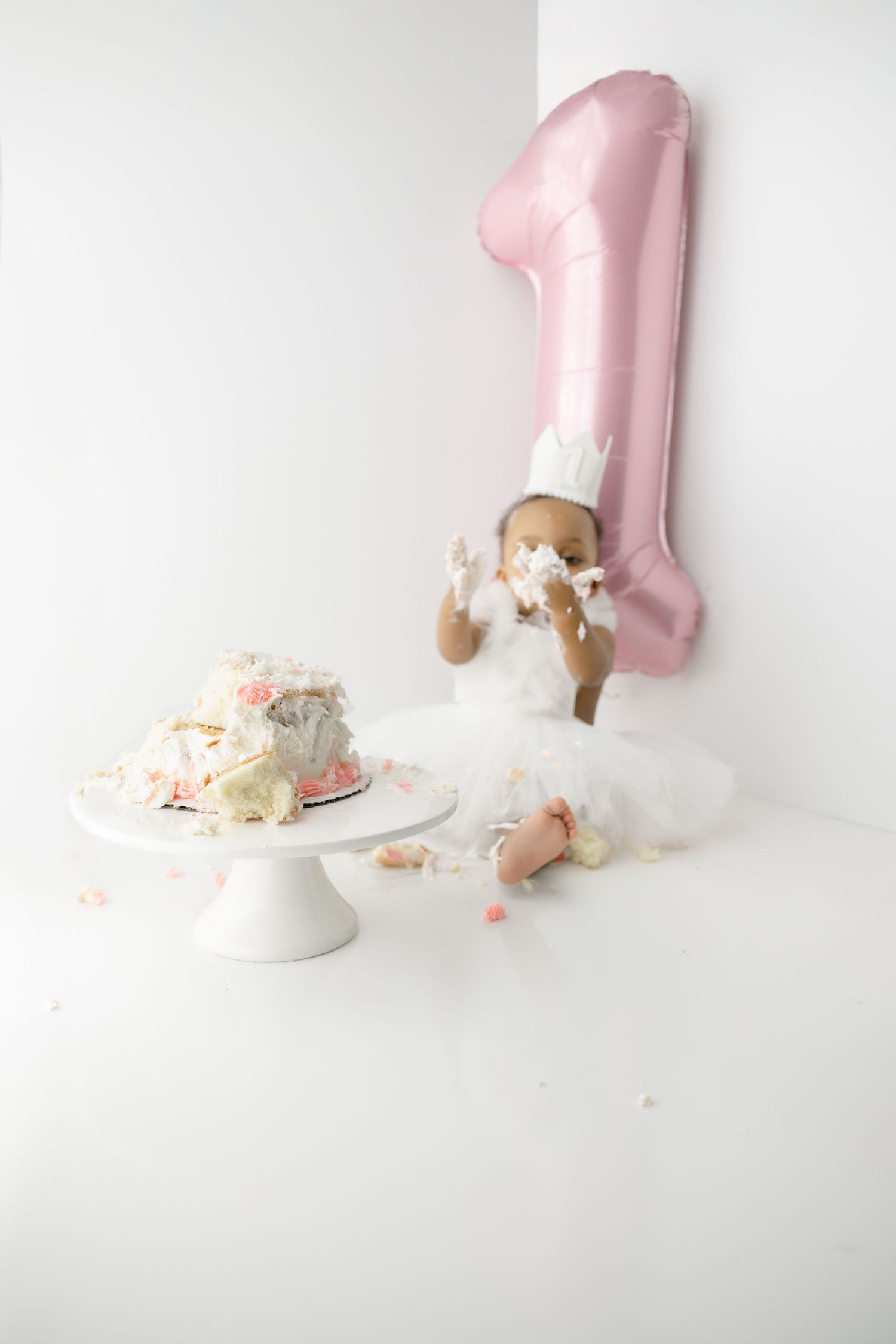 Pink smash cake photo session setup with decorated white cake, pink number one balloon, and white tulle backdrop.
