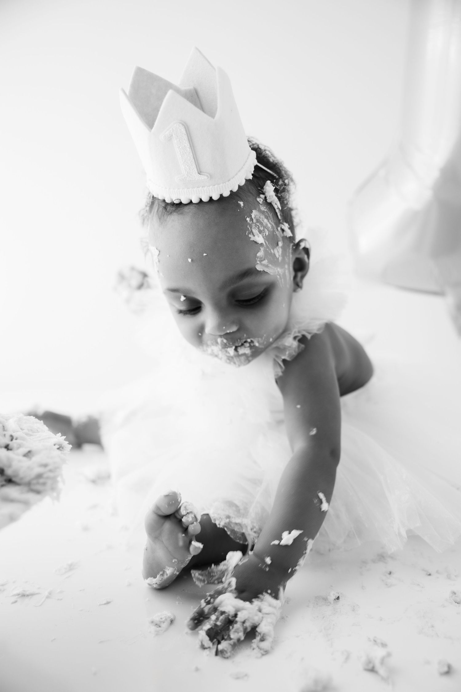 A series of black and white photos capturing a baby's first birthday cake smash session with messy frosting and cake.