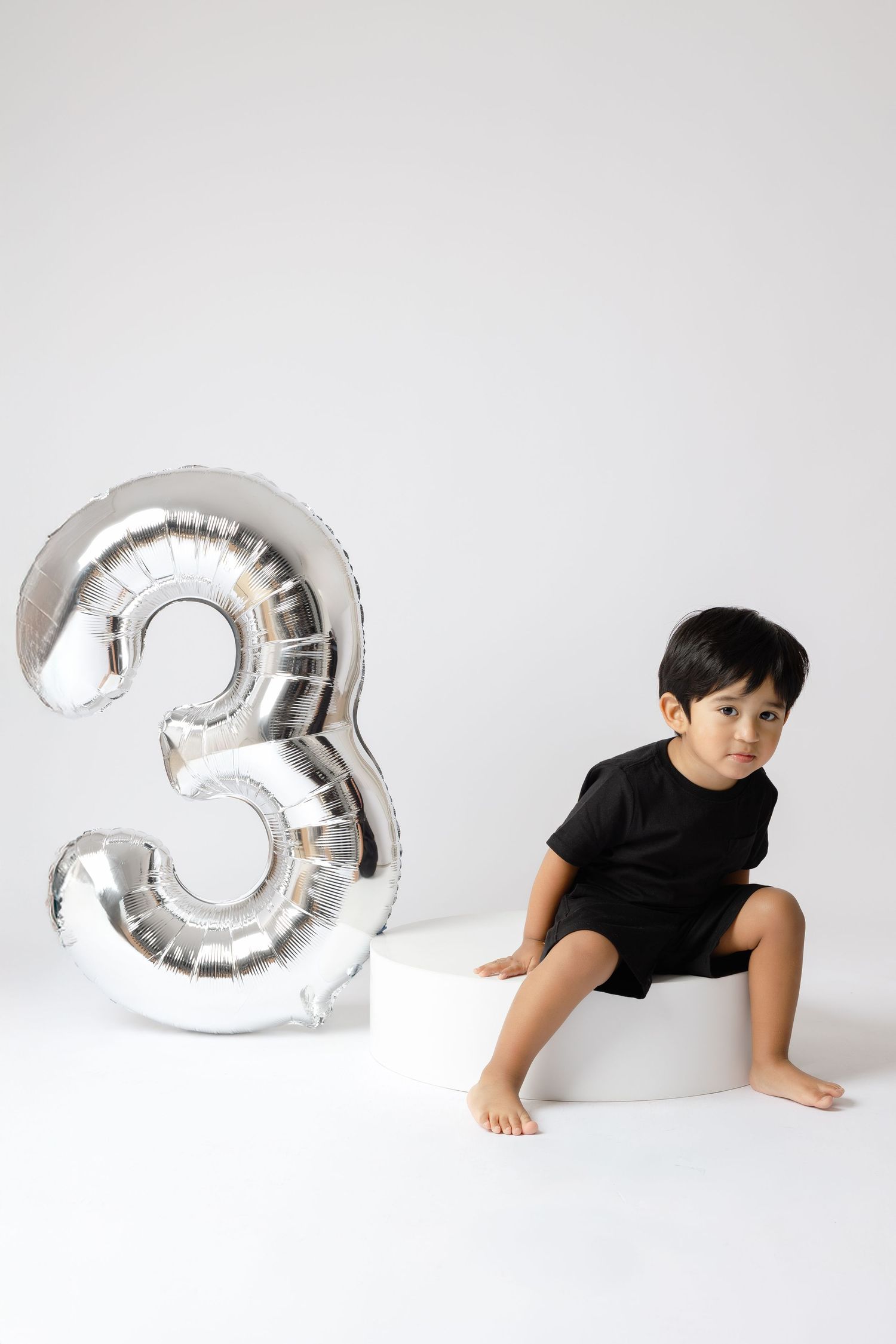 A silver metallic number 3 balloon shown in four progressive shots with someone in black interacting with it against white.