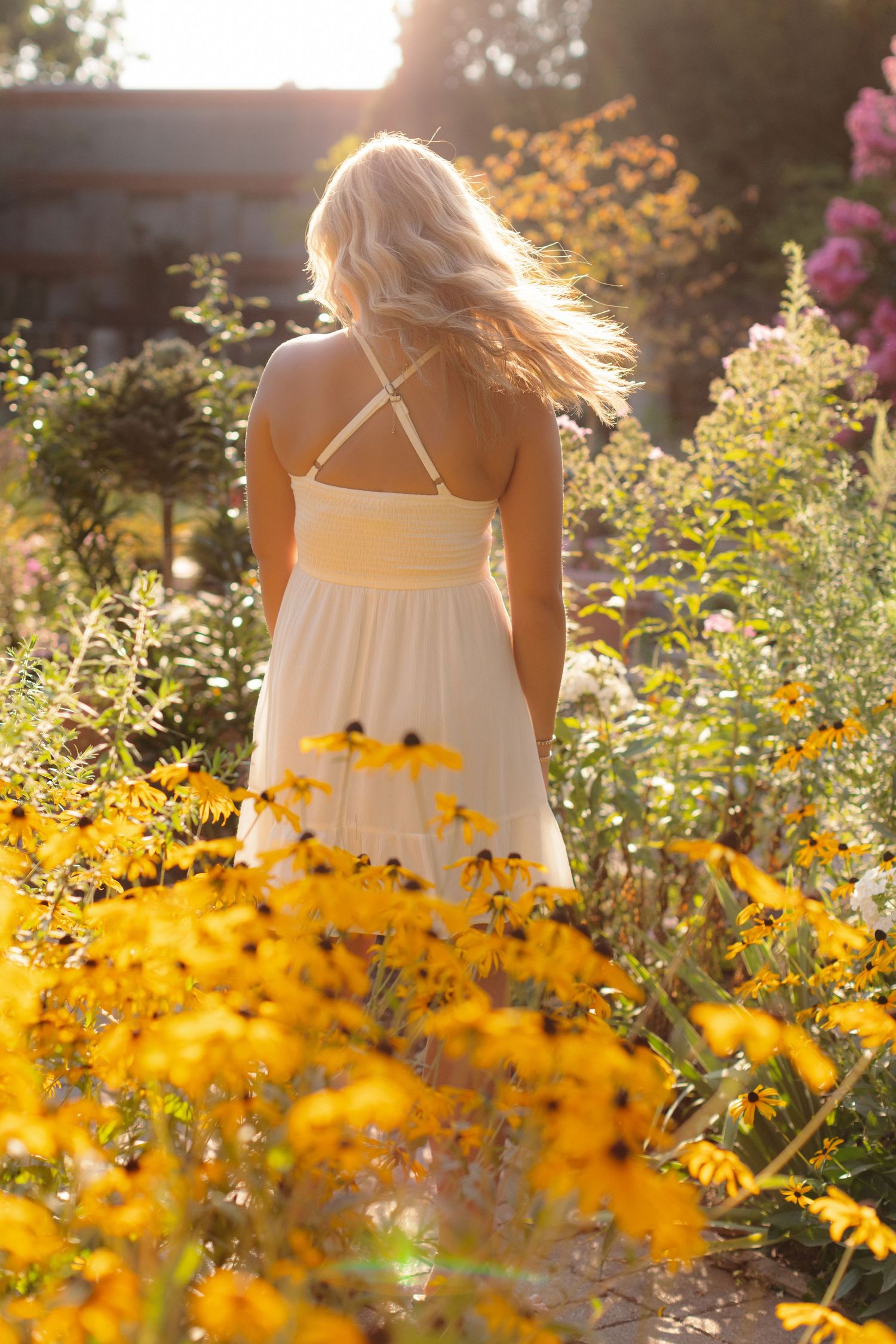 Person in white sundress stands among blooming yellow wildflowers during golden hour sunset.
