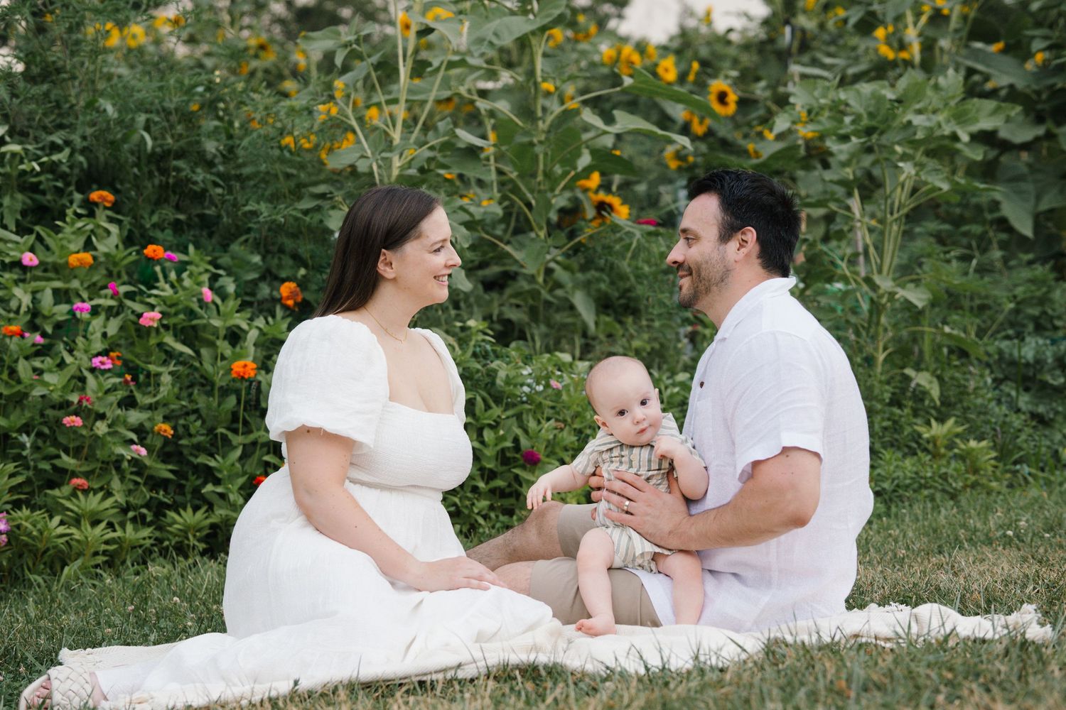 Family wearing white sits on blanket together for outdoor portrait with wildflowers in Cherry Hill, NJ.