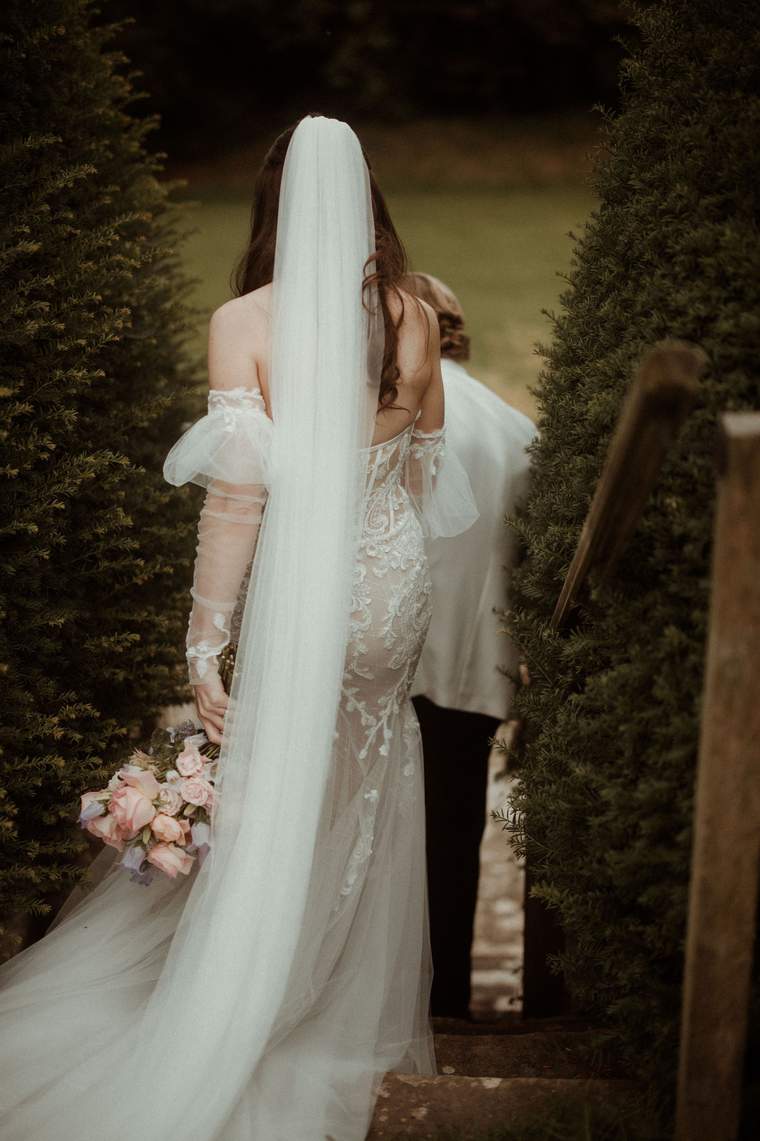 Ethereal bridal portrait showing flowing white wedding dress and veil against evergreen forest backdrop at Askham Hall.