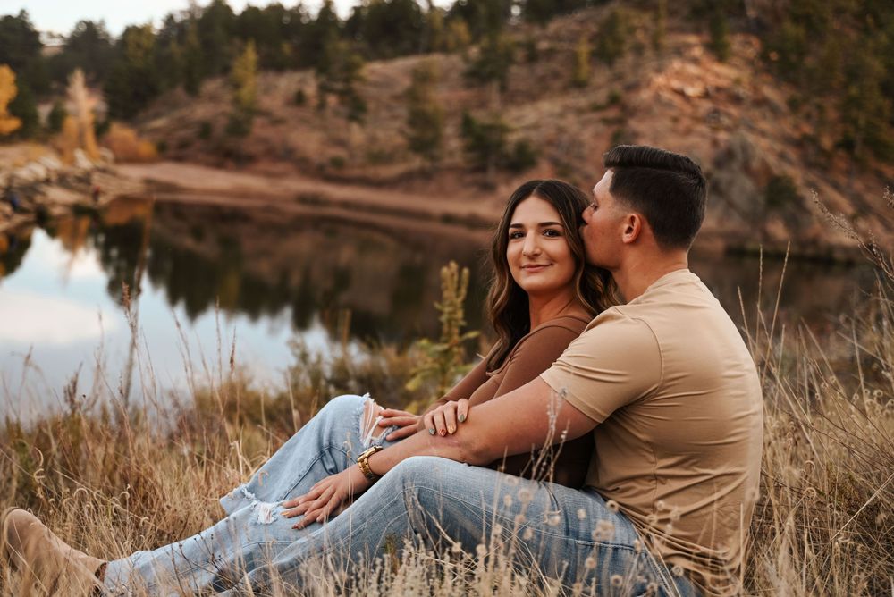 Romantic autumn engagement session by a serene lake with warm earth tones and natural scenery.