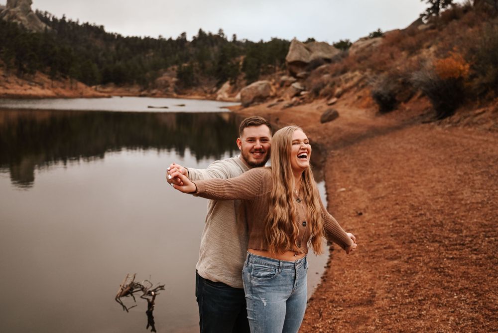 Couple sharing intimate moments on rocky terrain near a peaceful lake during golden hour.