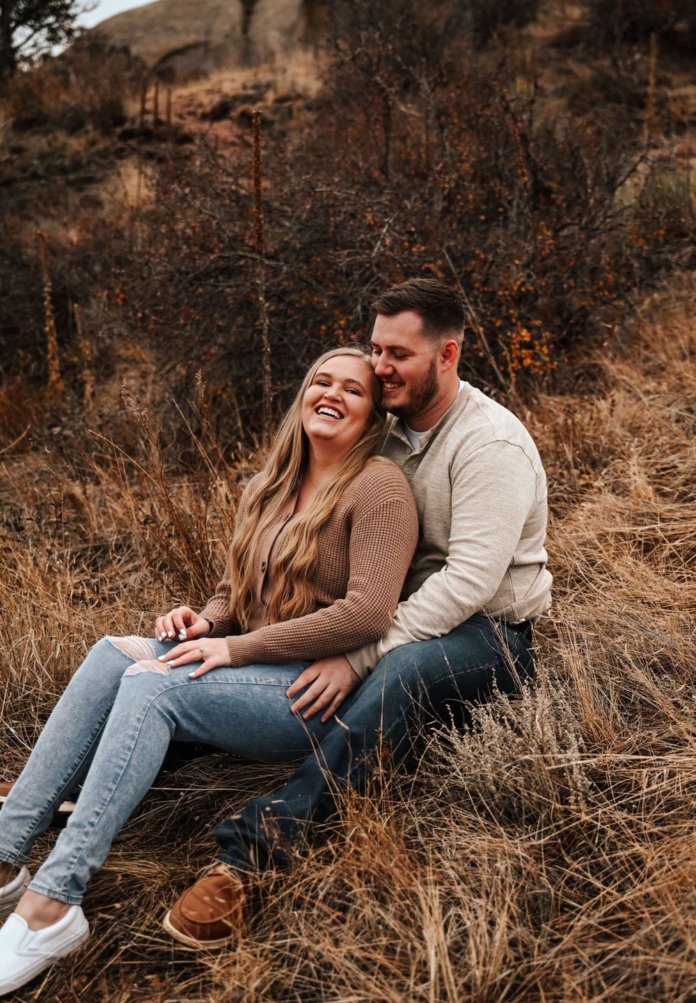 Candid engagement photos in autumn grass showing genuine laughter and connection.
