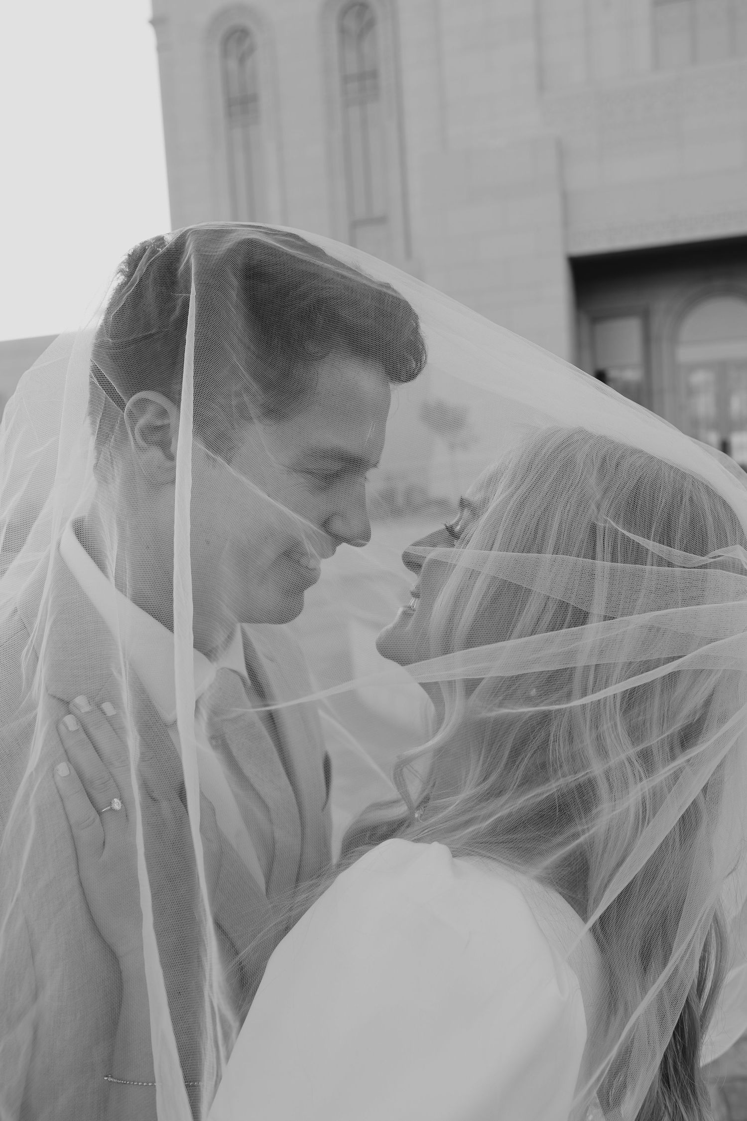 Black and white portrait of couple sharing intimate moment under bridal veil.