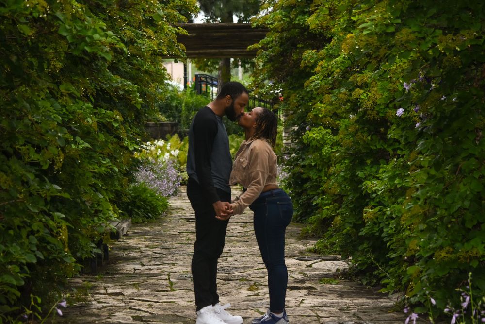 A romantic couple embraces on a stone path surrounded by green foliage and trees.