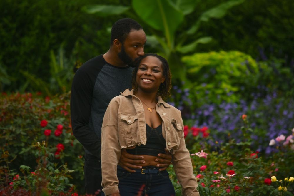 A happy couple enjoys a playful moment in a colorful garden with red and purple blooms.