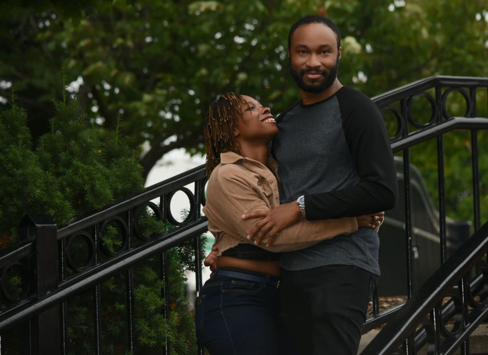 A couple shares an intimate moment on decorative metal stairs in a garden setting.