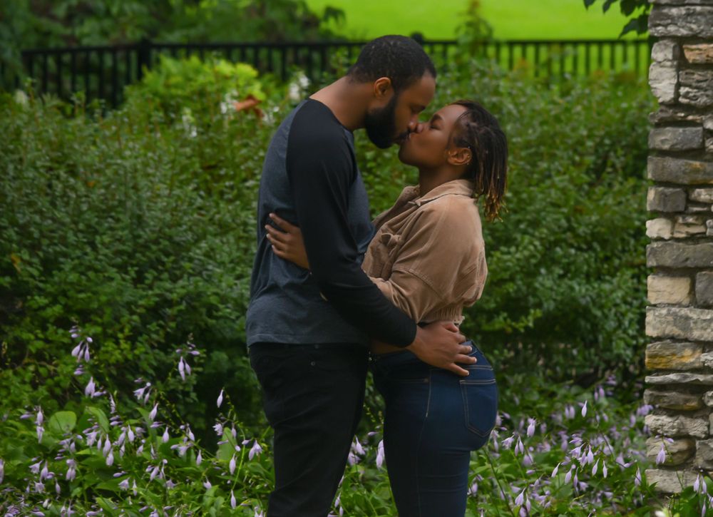 A tender moment between a couple embracing near stone walls and purple flowers.