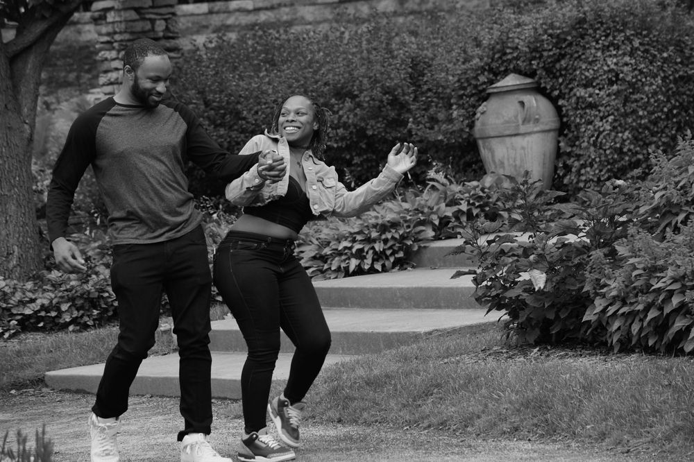 A couple dances and laughs together in a garden setting captured in black and white.