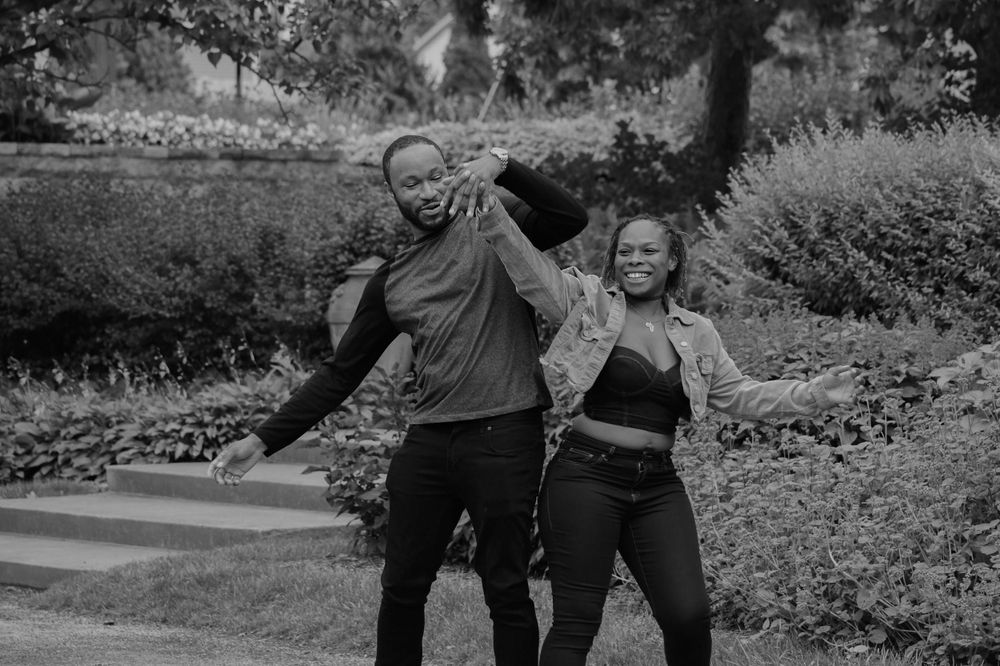 A playful couple strikes dynamic poses in a black and white garden photo.