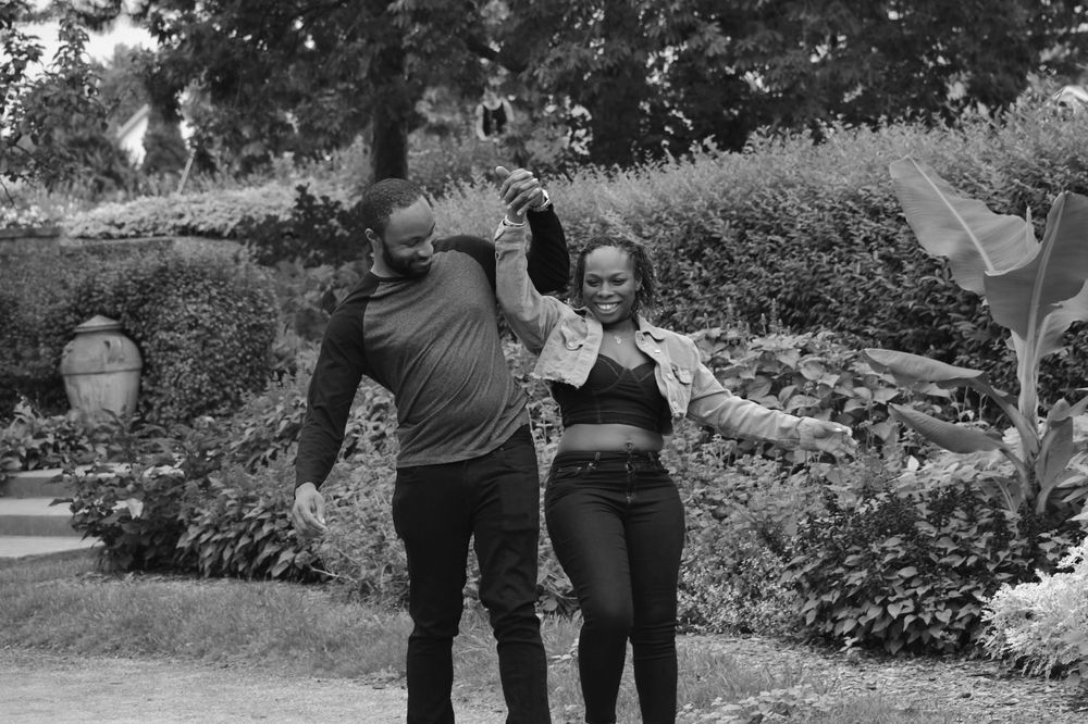 A couple dances and celebrates in a garden setting in black and white.