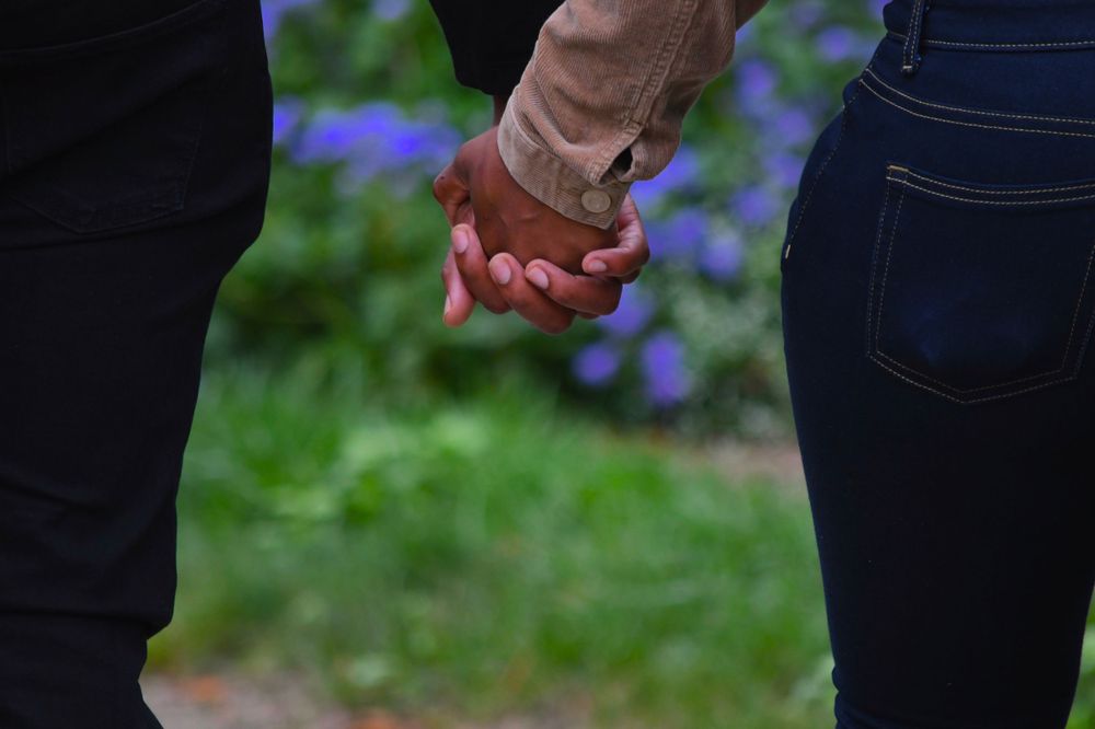 Close-up of two people holding hands with purple flowers in the background.