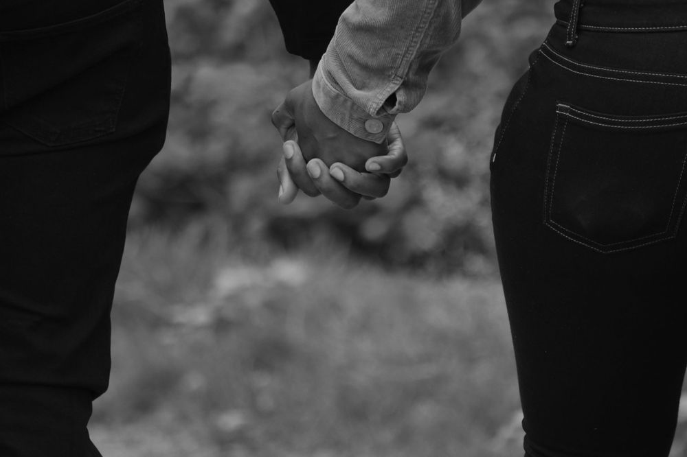 An intimate black and white shot of two people holding hands.