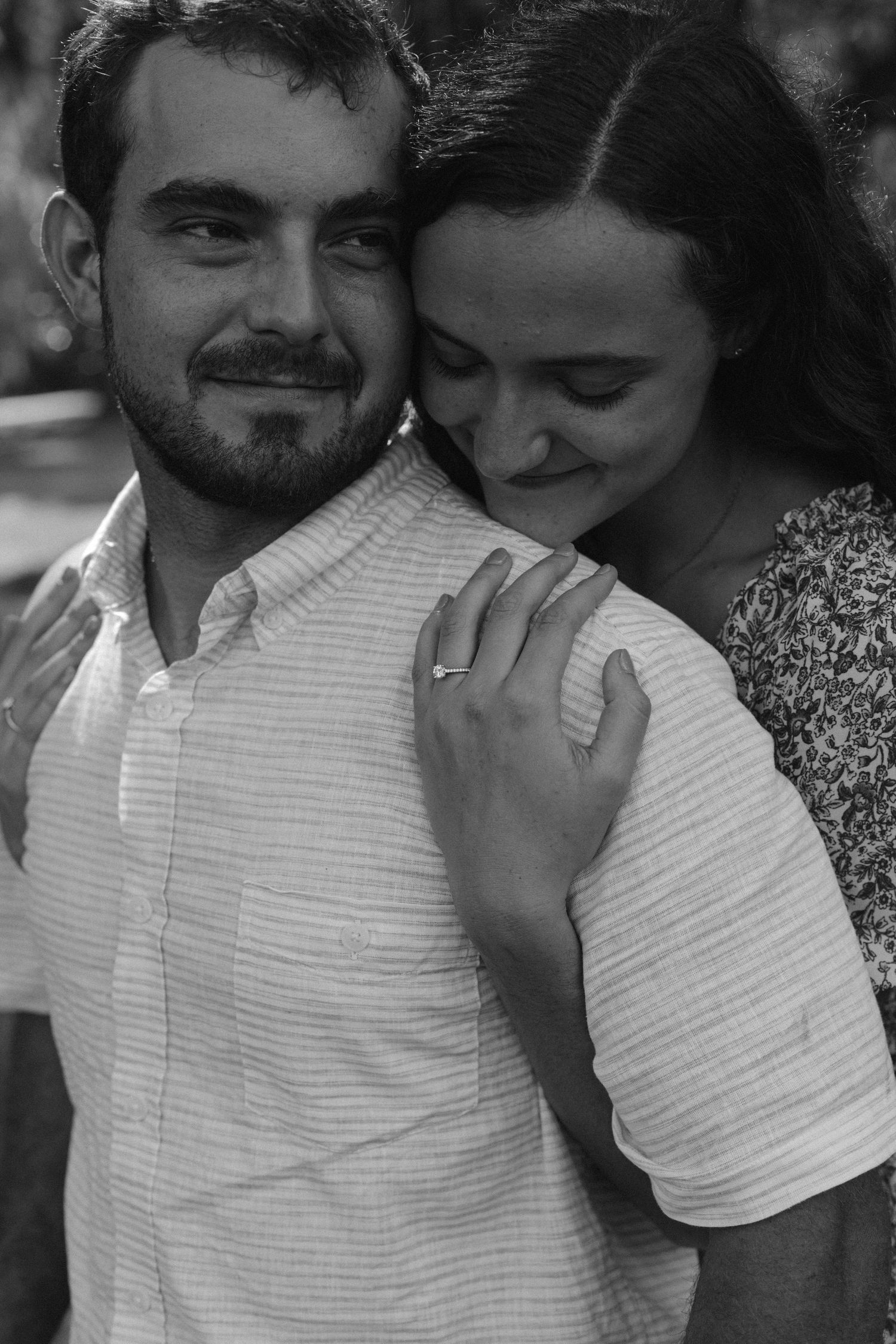 A black and white intimate portrait of a couple sharing a tender moment outdoors.