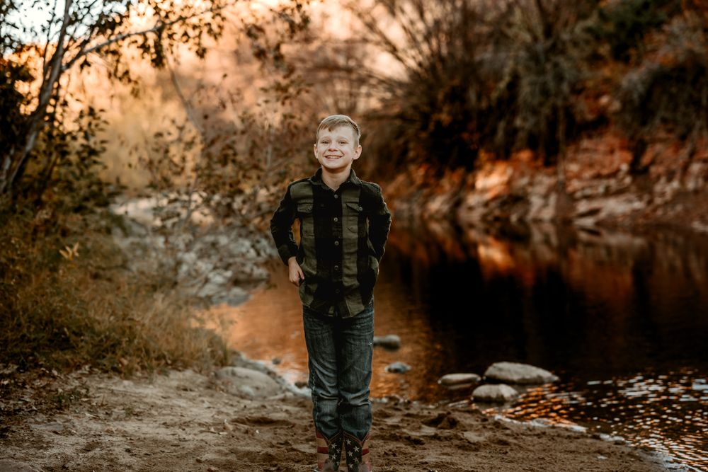 Autumn outdoor portrait session along rocky riverbank at sunset.