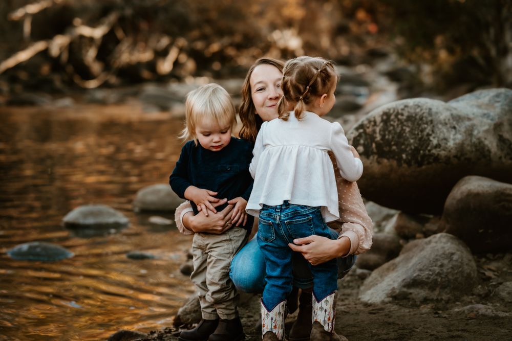 A family sitting together on rocks by a stream during sunset.