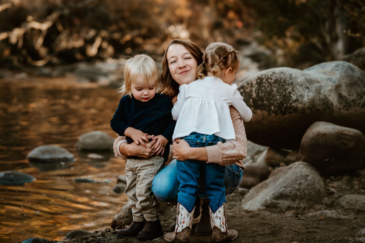 A sweet family moment captured on rocky terrain near water at golden hour.