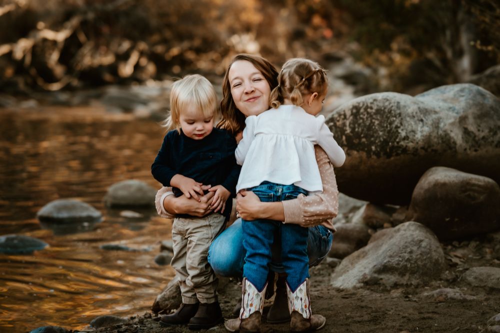 A sweet family moment captured on rocky terrain near water at golden hour.