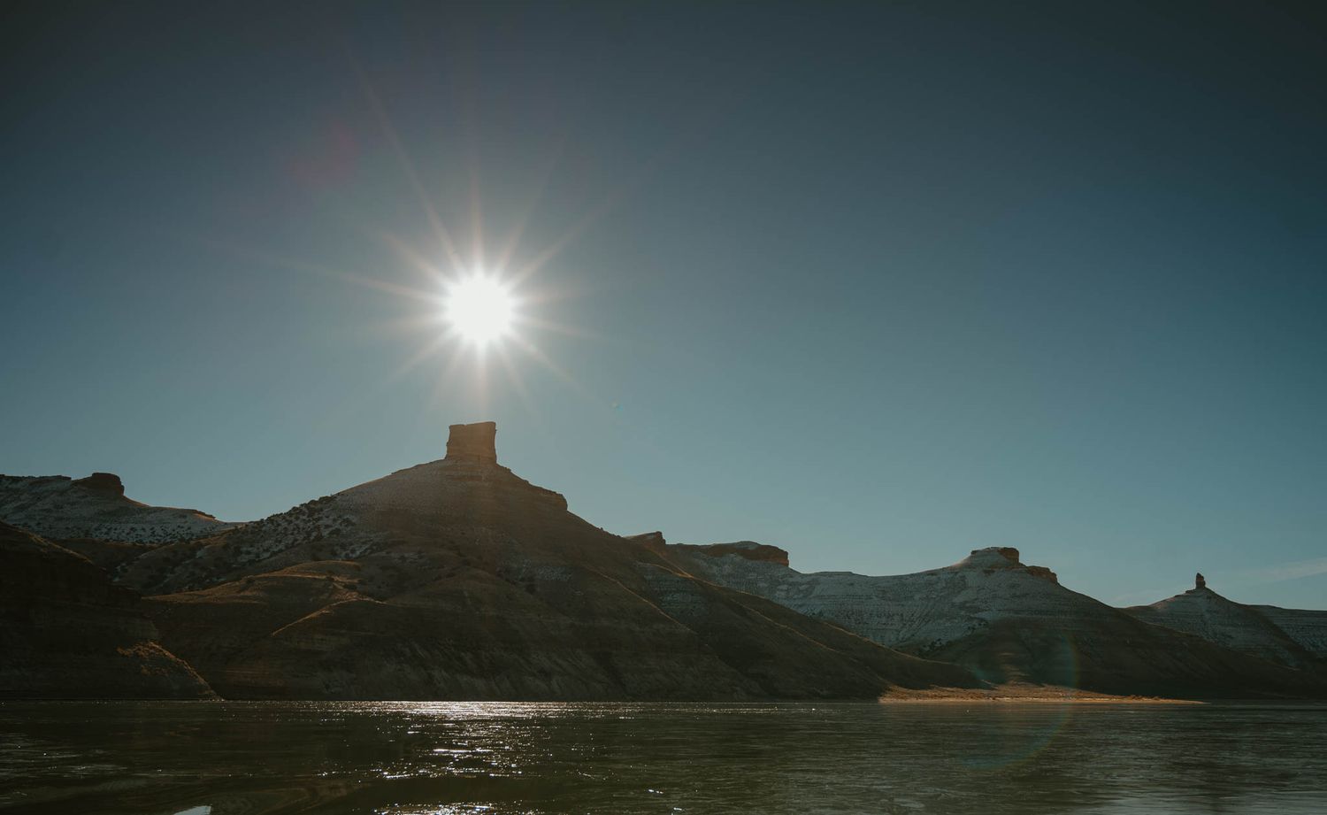 Dramatic mountain silhouettes against bright sunburst in a turquoise sky.