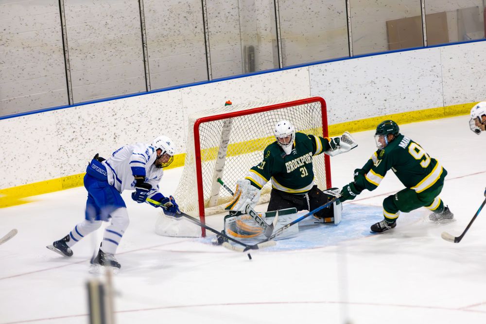 Hockey player attempts shot on goal while defenders try to block.