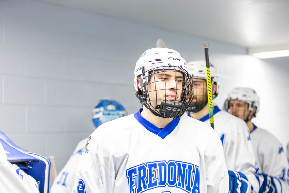 Hockey team members in Fredonia jerseys gather in the locker room before a game.