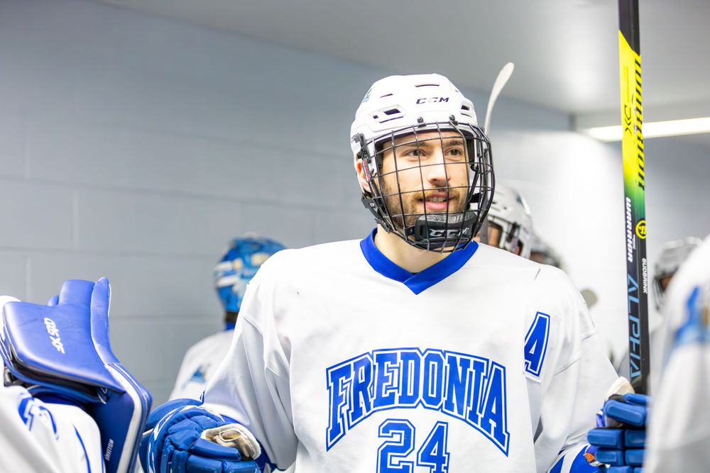Hockey players in Fredonia blue and white uniforms prepare for a game in the locker room area.