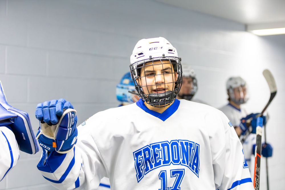 Players in Fredonia hockey uniforms congregate in a brightly lit corridor.
