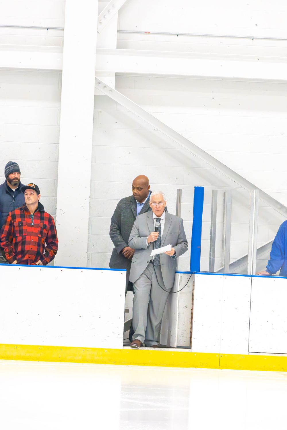 Spectators in winter clothing watch from above the hockey rink boards.