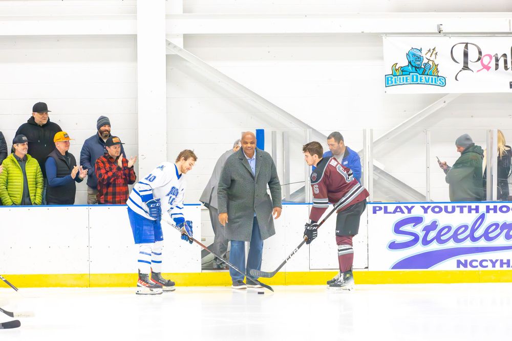 Wide view of hockey players and spectators around an indoor ice rink during a game or practice.