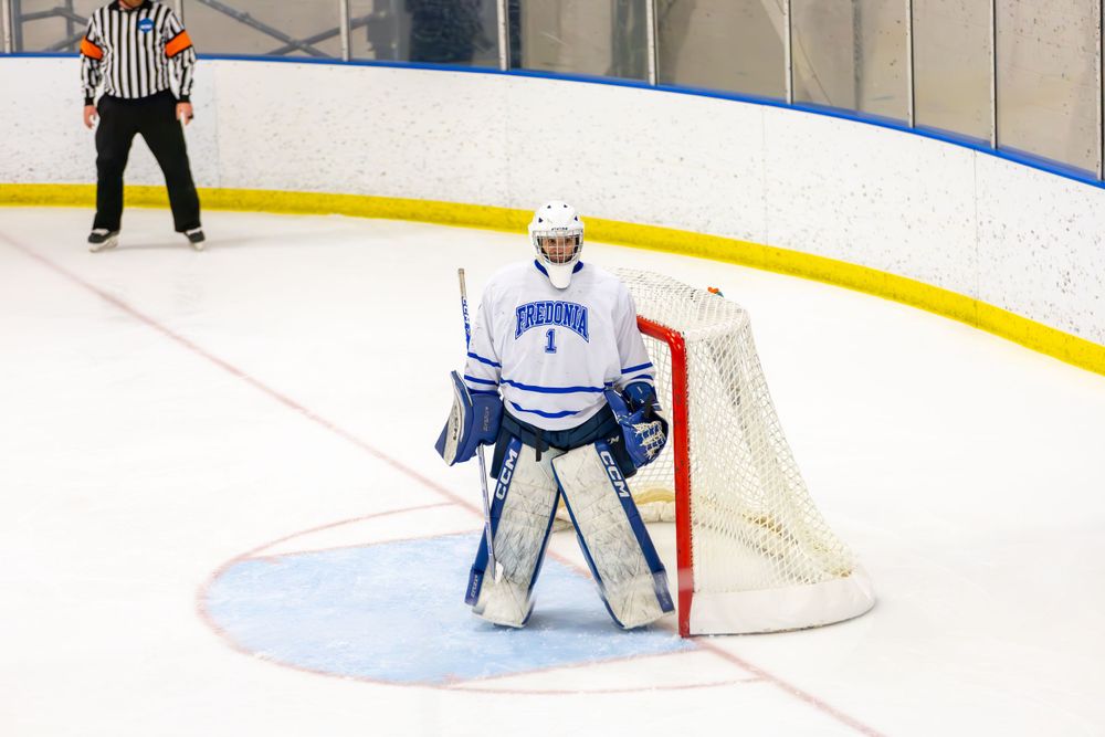 Hockey goalie in white uniform defends the net during practice or game.