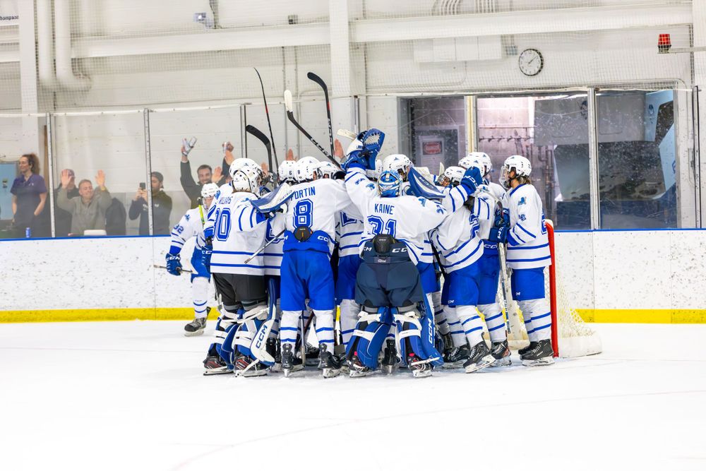 Hockey players in blue and white uniforms stretch on the ice during a pre-game warmup session.