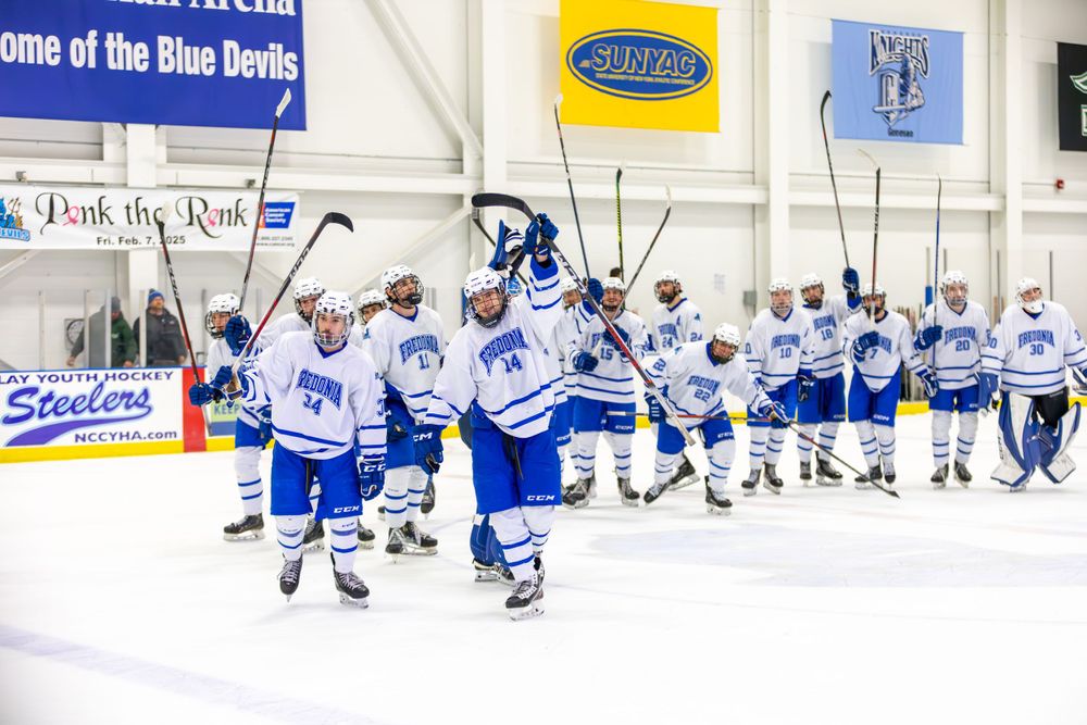 Hockey team in blue and white jerseys performs stretching exercises on the ice rink.