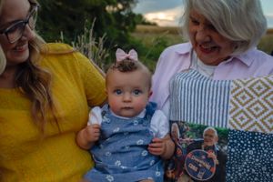 A baby wearing a blue outfit and bow being held in a casual outdoor setting.