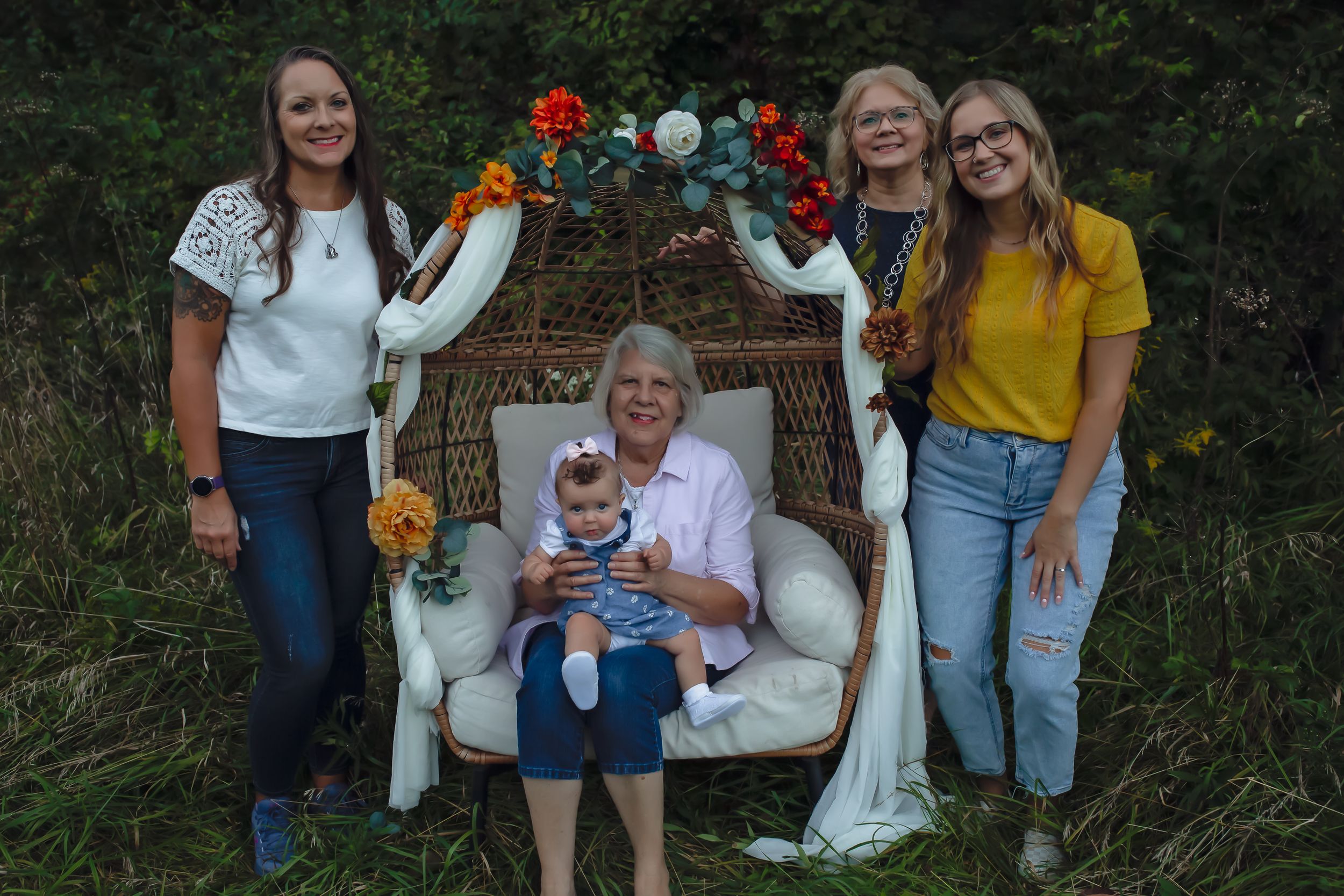 Multi-generational group poses on a wicker chair decorated with flowers and white fabric outdoors.